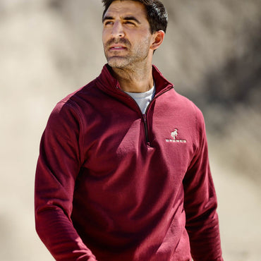 Man wearing a red pullover with a brand logo against a blurred natural background