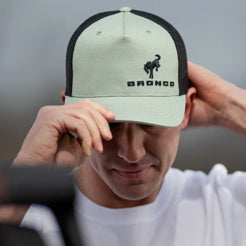 Person wearing a Bronco cap with a logo on a neutral background